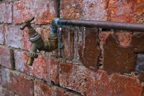 Outdoor faucet on a brick wall with icicles hanging from the pipe