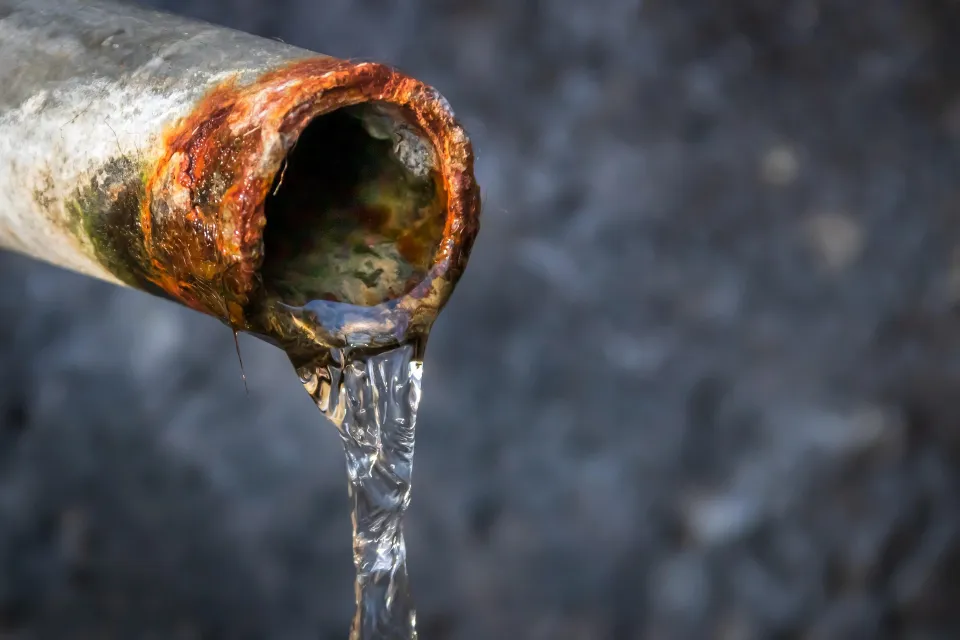 Rusty metal pipe with water dripping from its open end