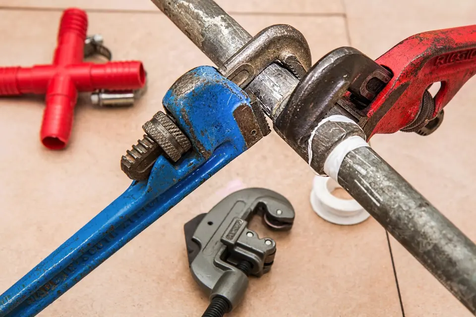 Pipe wrenches and a pipe cutter beside a metal water pipe